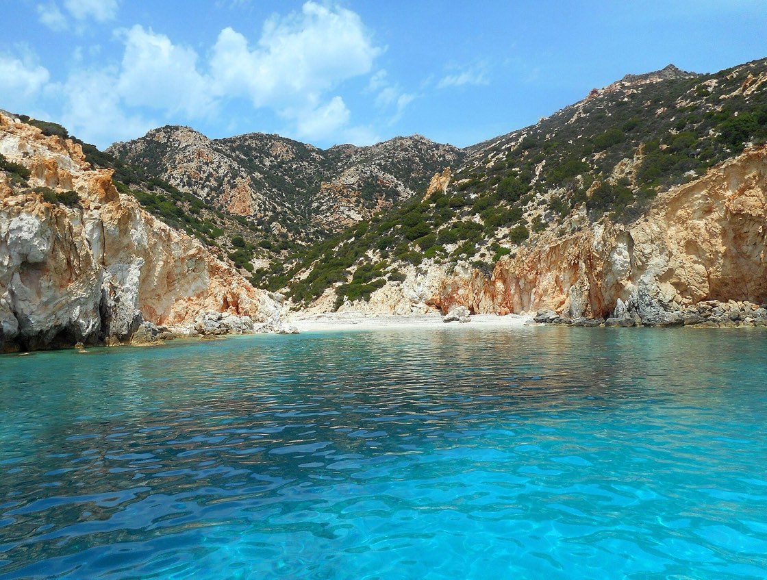 A turquoise cove and white beach below the colourful cliffs of Polyaigos